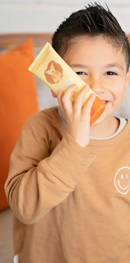 Un niño sonriente con un tubo de Taming Gel junto a la cara