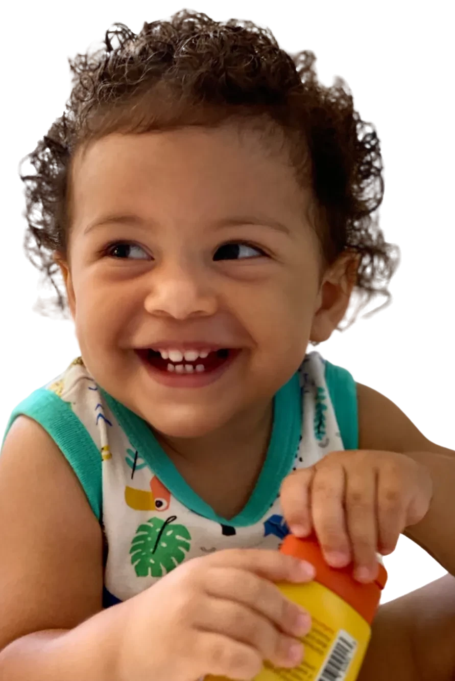 A laughing toddler with curly hair holding a tube of Taming Cream