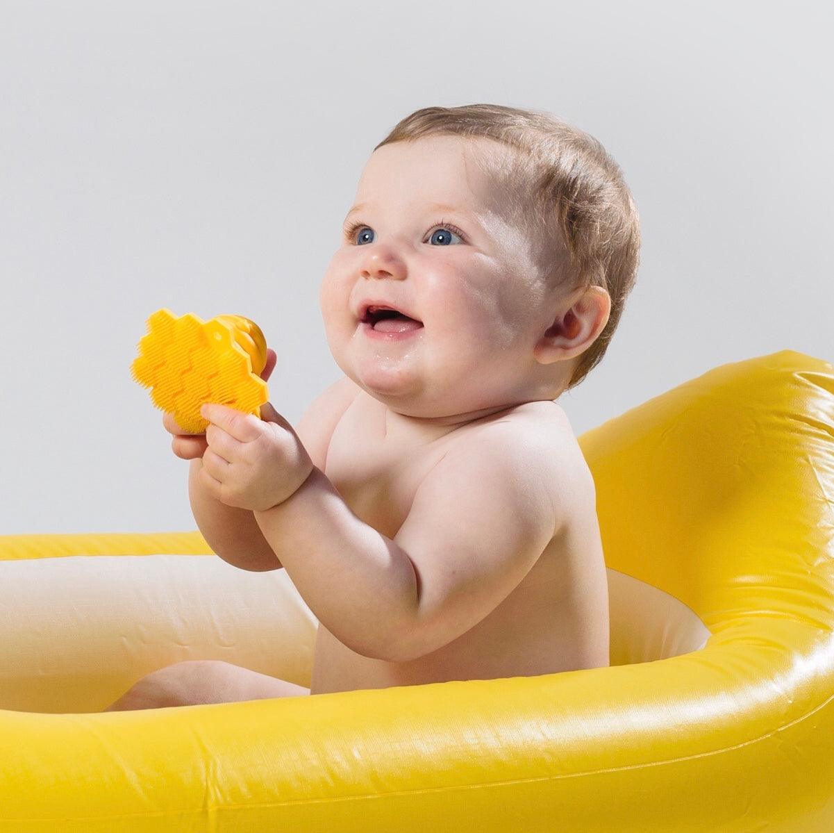 A baby sitting in a small tub with the Bath ScruBEE