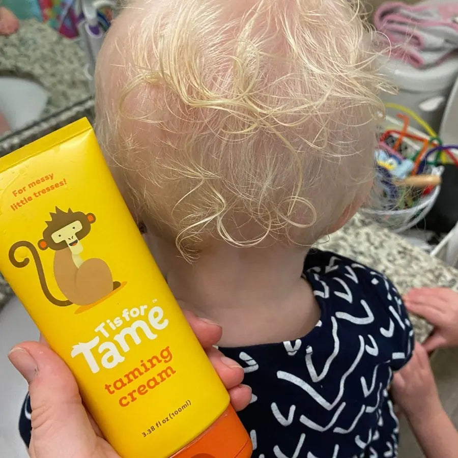 A toddler with blonde curls next to a tube of Taming Cream