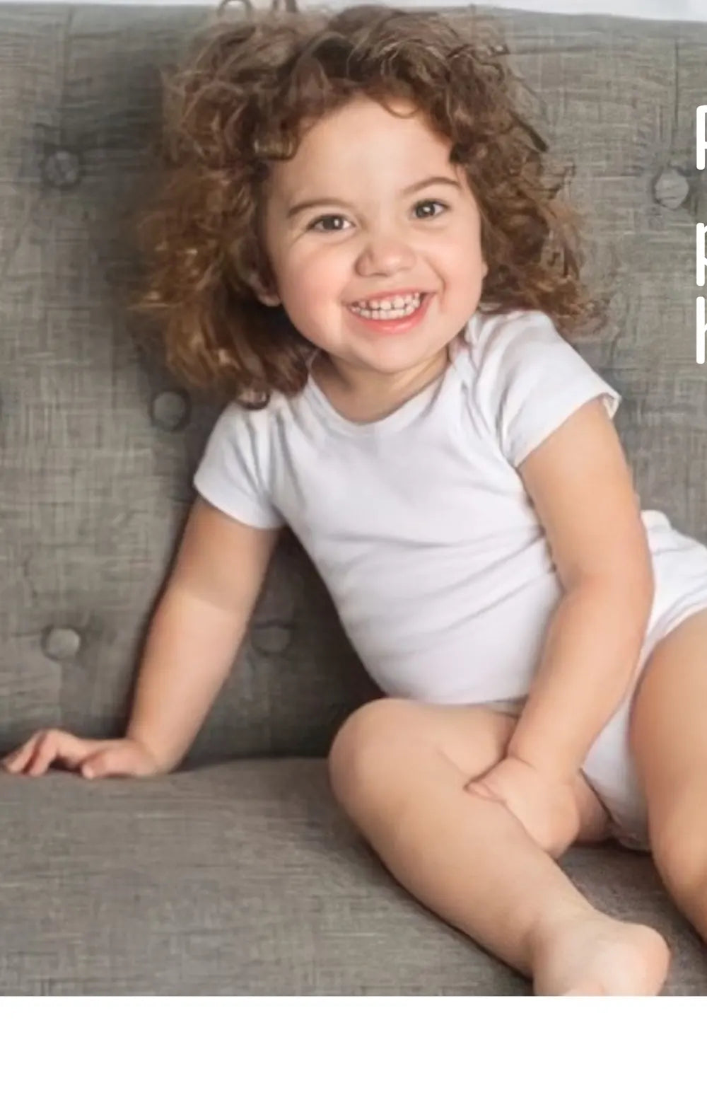 A curly-haired toddler laughing on a grey couch